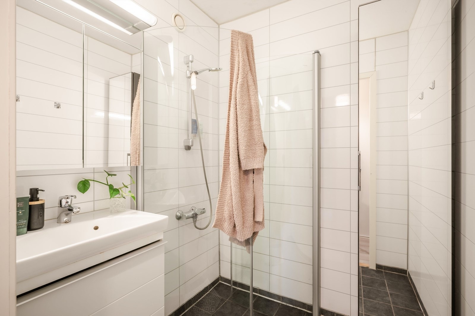 Lyst og fint baderom innredet med servant med underskap, innfellbare dusjvegger og speilskap både over servant og på vegg. Galleribilde