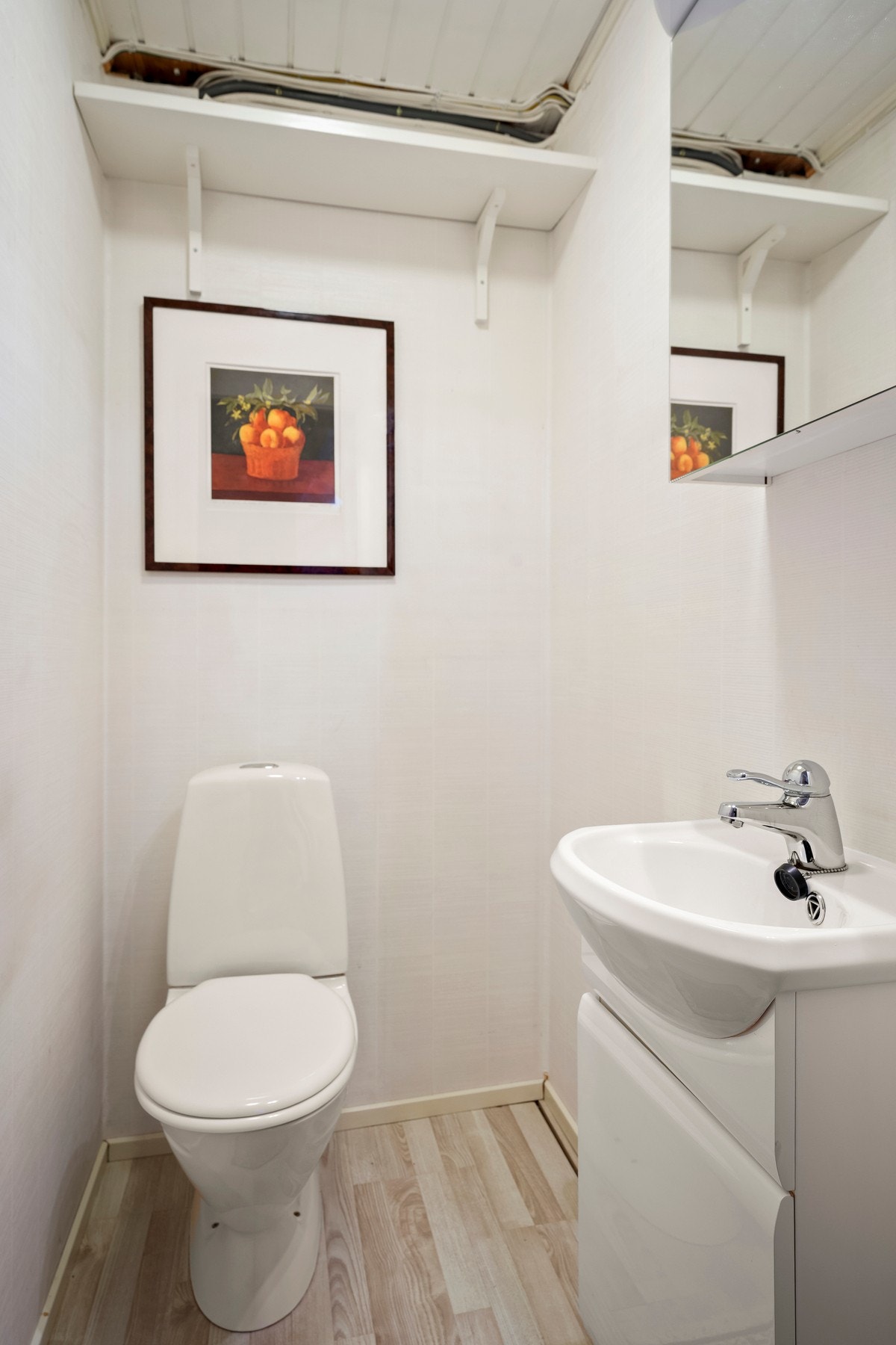Wc i underetasjen har laminat på gulv, tapet på vegger og malt panel i tak. Galleribilde