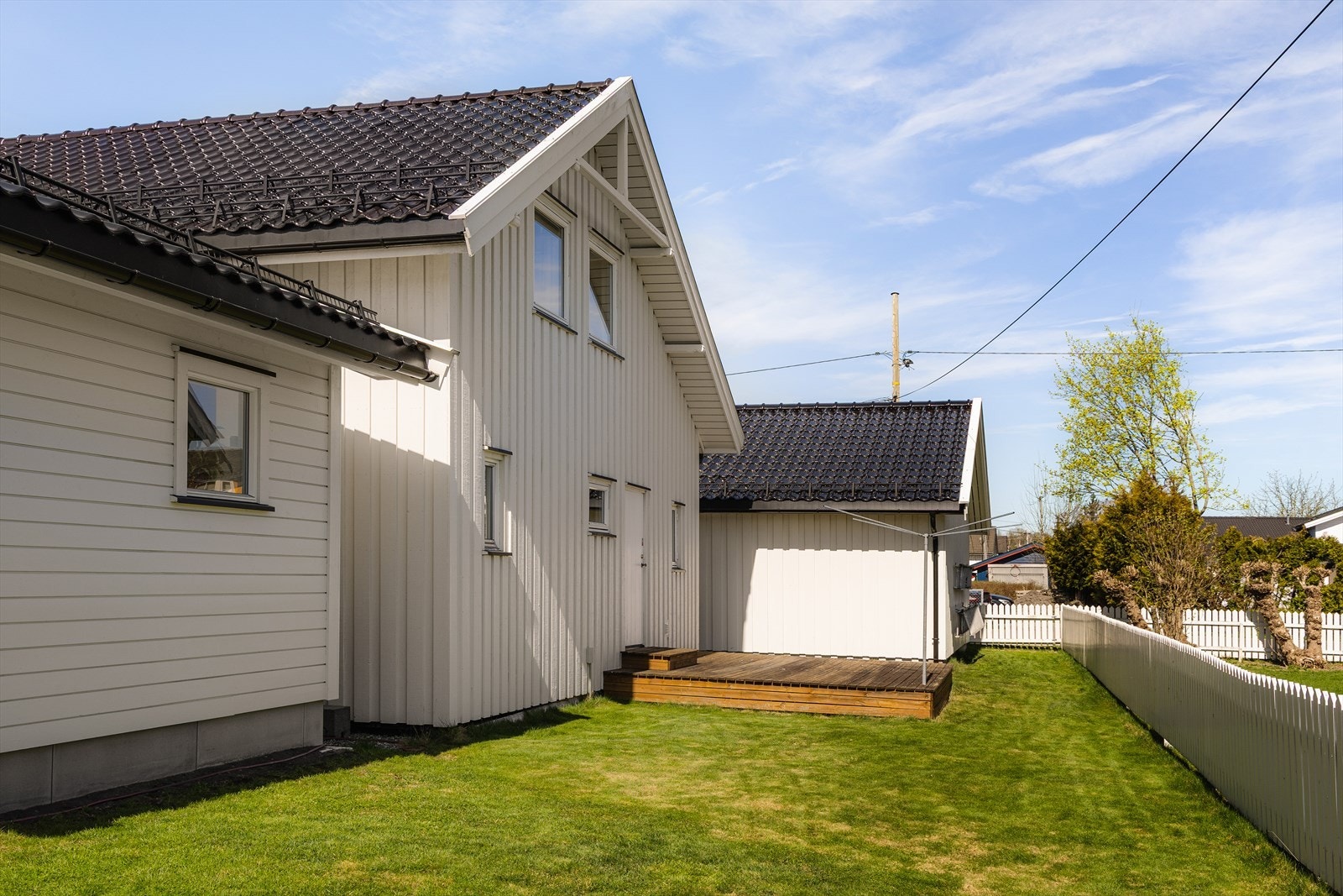 Ved inngangen til vaskerommet er det bygget en fin platting, og satt opp tørkestativ. Eiendommen er pent rammet inn med hvitmalt gjerde. Galleribilde
