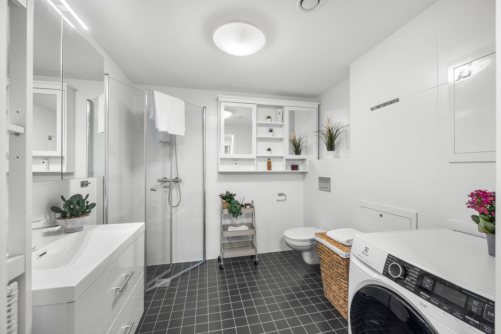 Baderom med flislagte overflater på gulv og vegger, vegghengt toalett og opplegg for vaskemaskin. Galleribilde