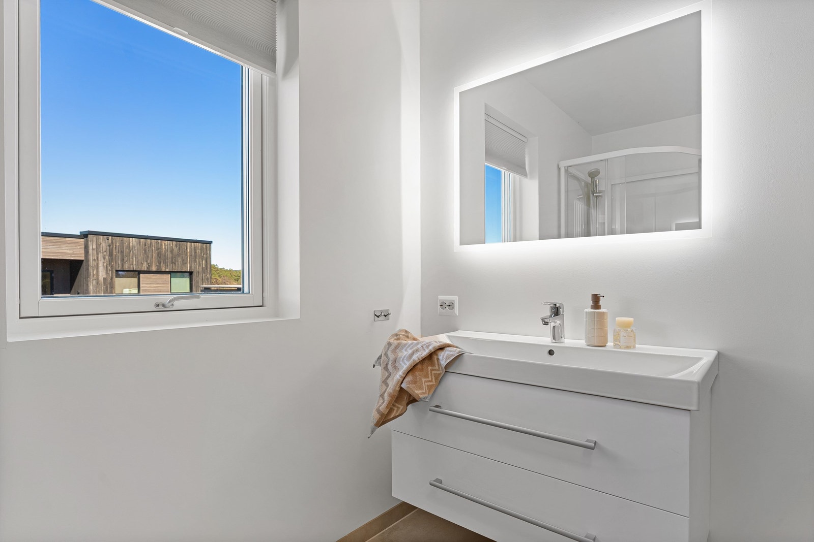 Stort vindu gir naturlig lys, ventilasjon, servant med oppbevaring og speil med lys som gir et moderne uttrykk Galleribilde