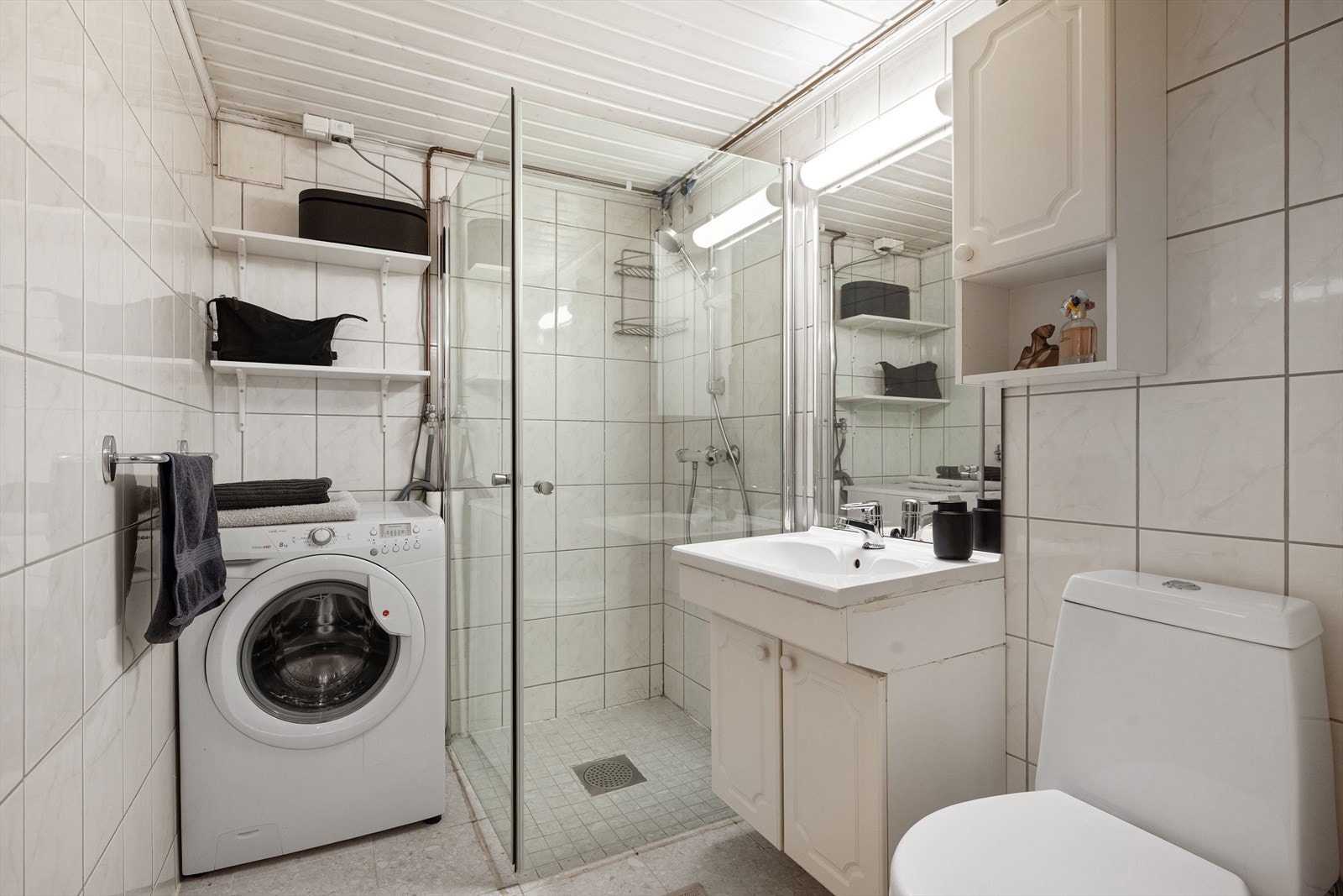 Det andre badet i kjelleren har fliser på gulv og vegger, dusj, toalett og opplegg for vaskemaskin. Galleribilde