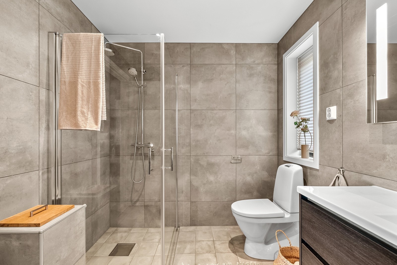 Badet har flislagte overflater, dusj med innfellbare glassdører, gulvvarme, downlights og innredning med god oppbevaringsplass. Galleribilde