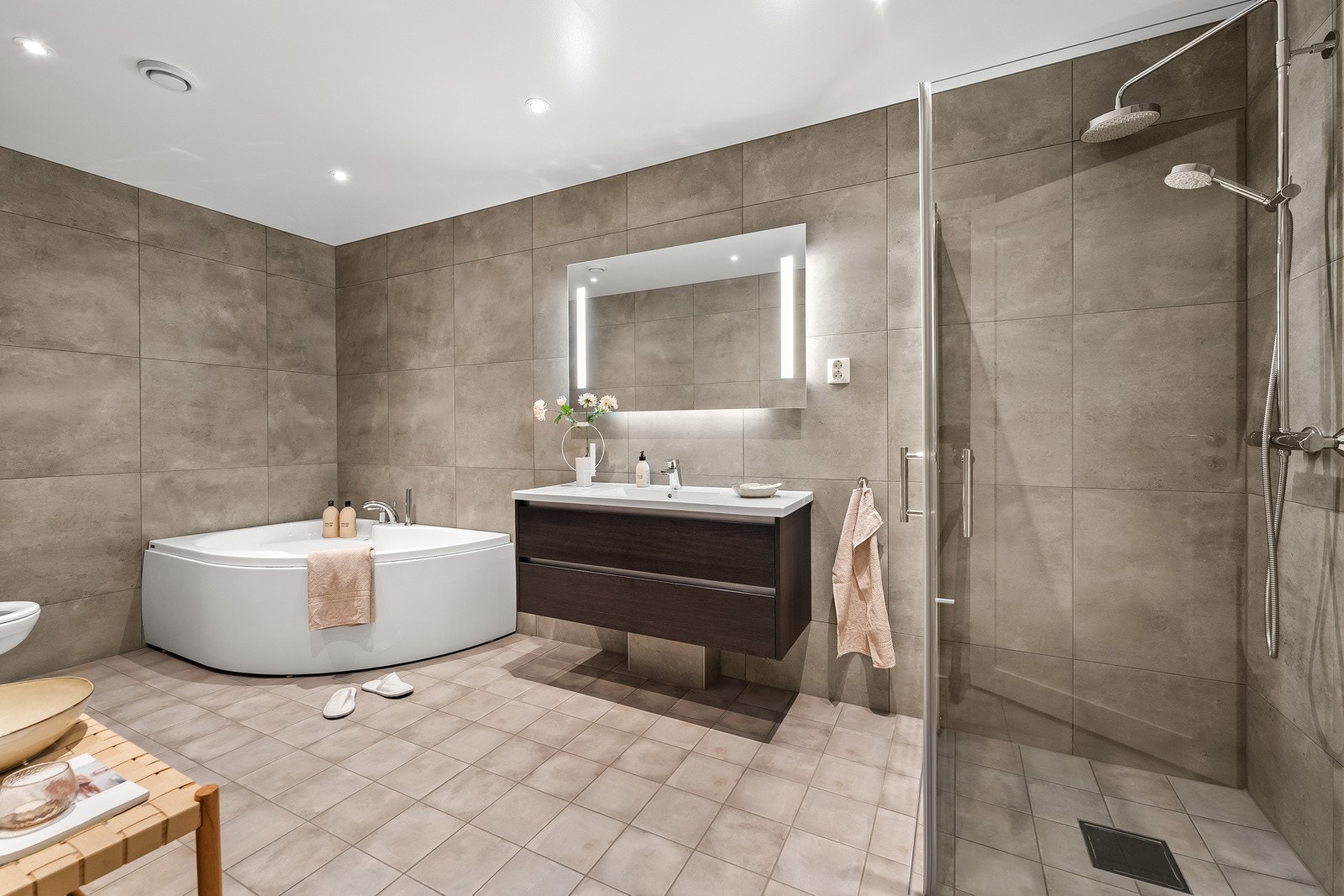 Badet er utstyrt med dusjhjørne, vegghengt toalett, dobbel servant med skuffeseksjon, speil med belysning, gulvvarme og downlights. Galleribilde