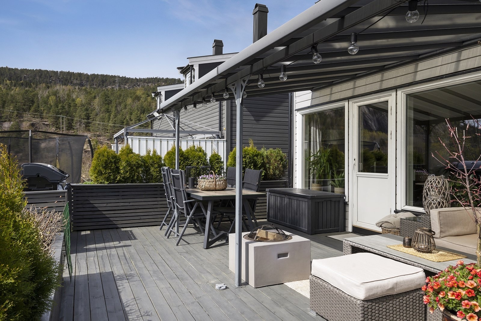 Skjermet terrassemiljø med overbygg, store flotte blomsterkasser og utgang fra boligen Galleribilde