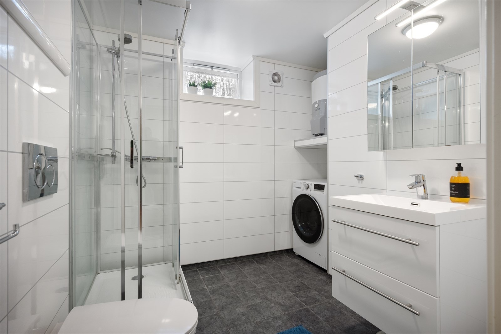 Romslig og funksjonelt baderom med behagelig gulvvarme. Badet er innredet med vegghengt toalett, dusjkabinett, servant med praktisk møblement, speil og belysning, samt opplegg for vaskemaskin. Galleribilde