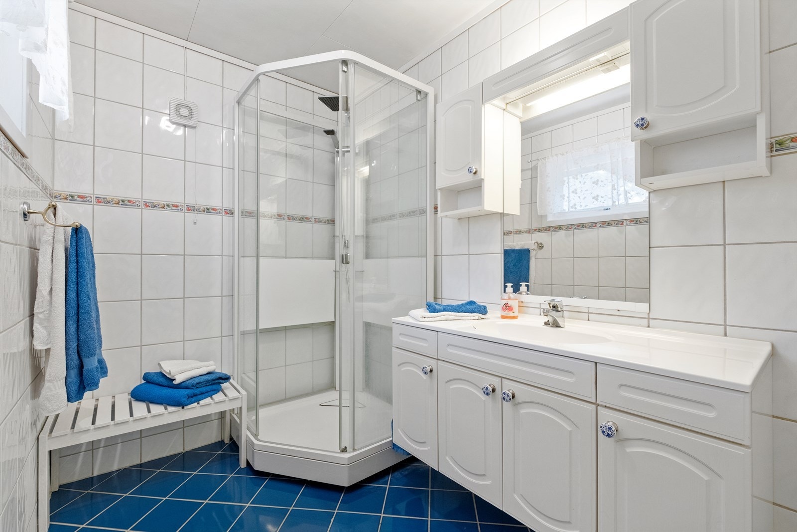 Badet har flislagte gulv og vegger, samt dusjkabinett og tilhørende baderomsinnredning. Galleribilde