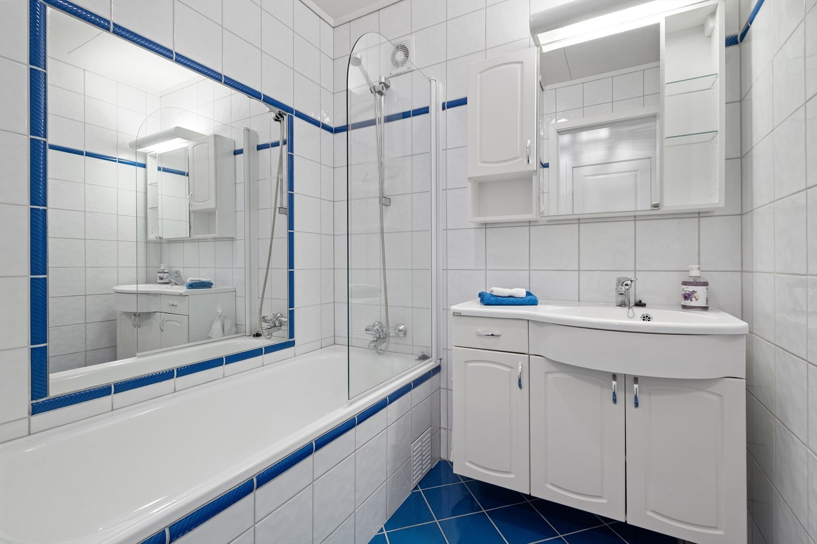 Rommet har hvite fliser på vegger, badekar og servant med speilskap. Galleribilde
