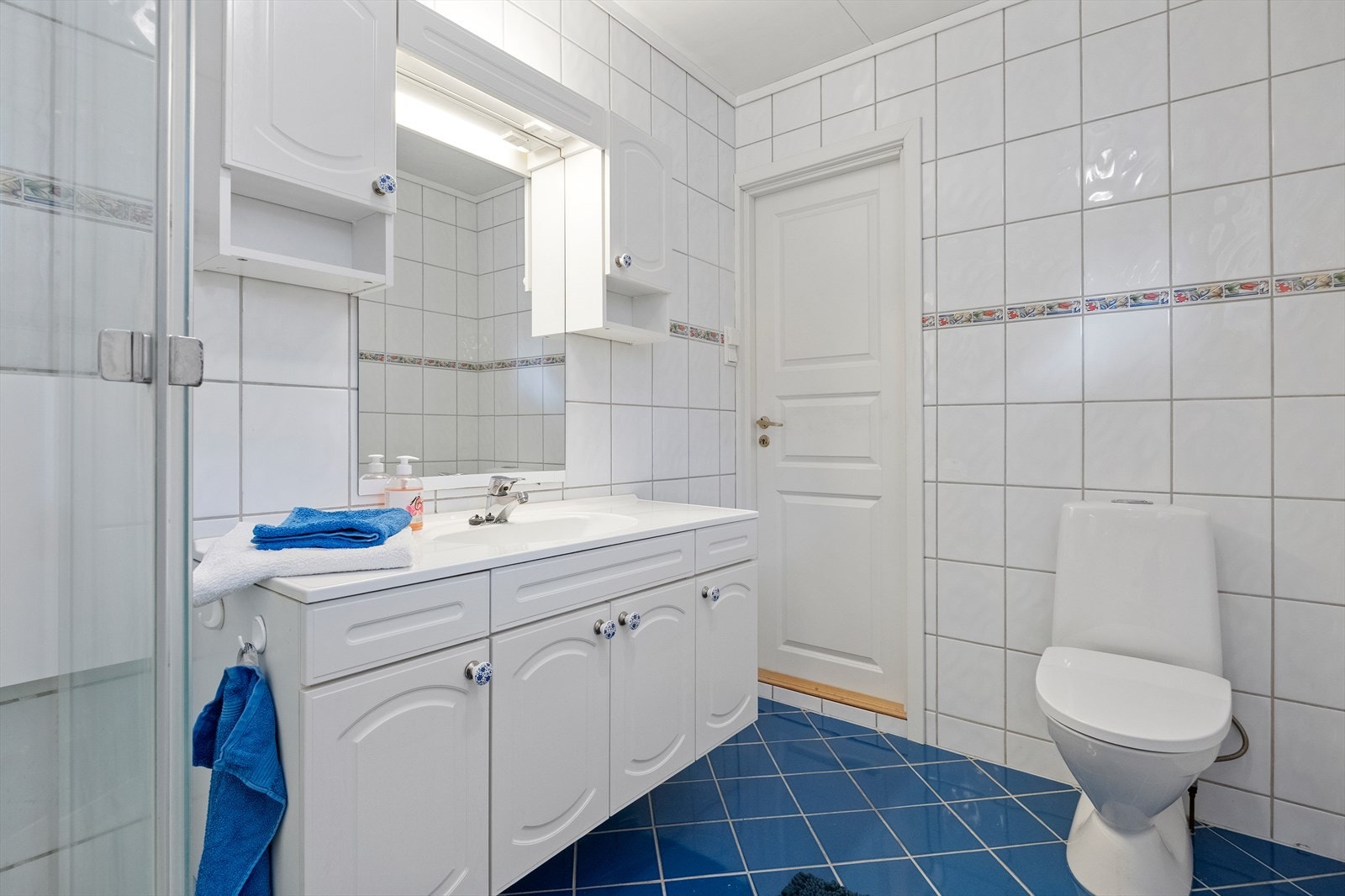 Badet er utstyrt med flislagte overflater, dusjkabinett og gulvmontert toalett. Galleribilde