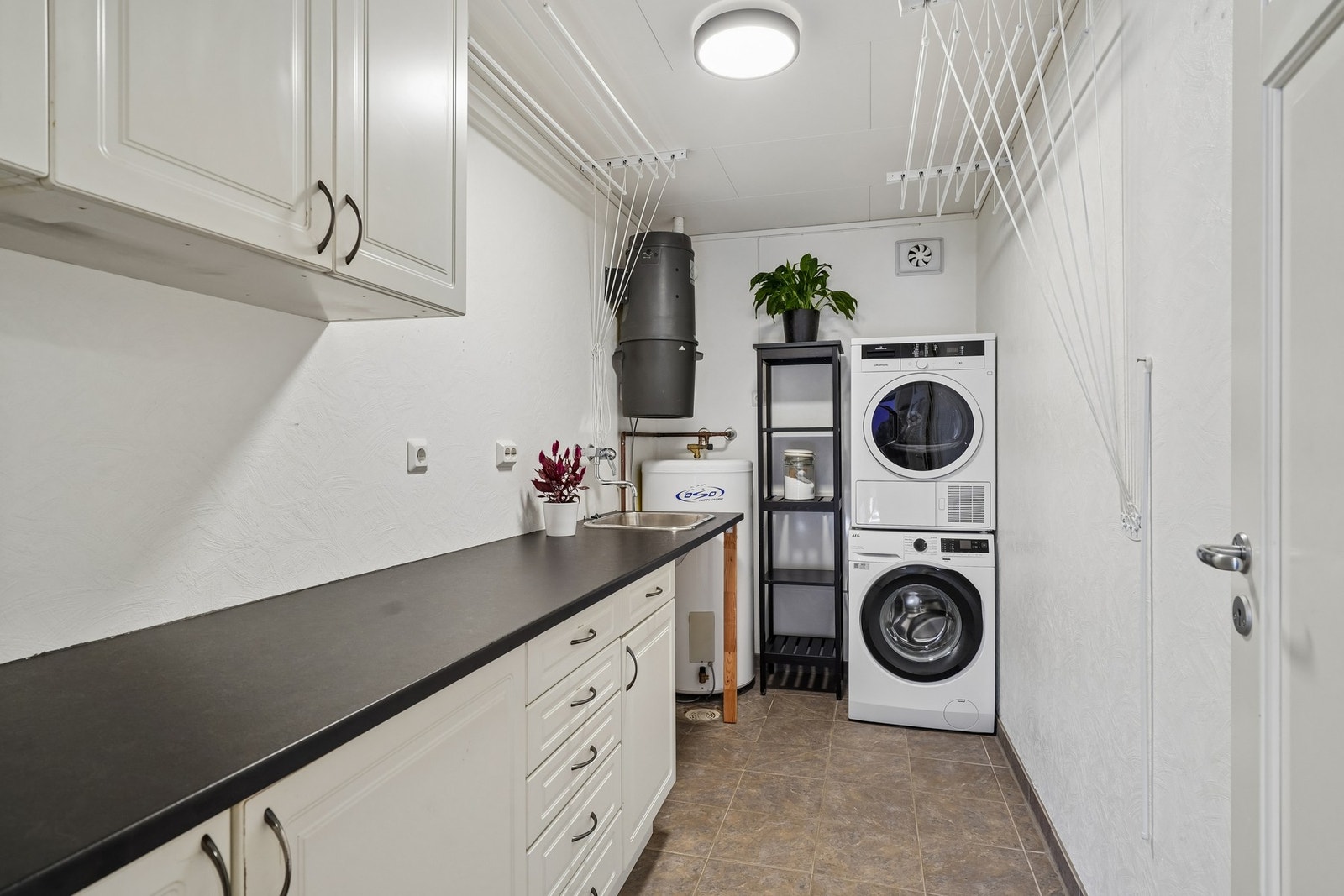 Innredet med vaskeromsinnredning med hvite profilerte fronter og laminat benkeplate med nedfelt stål skyllekum. Opplegg for vaskemaskin og tørketrommel. Galleribilde