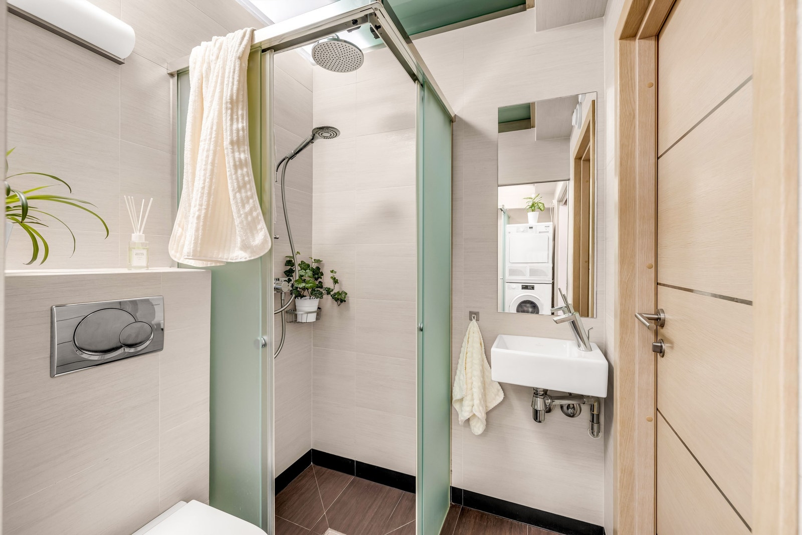 Badet nærmest gangen er innredet med vegghengt toalett og dusjnisje i frostet glass, to-greps dusjarmatur på vegg og regnfallsdusj Galleribilde