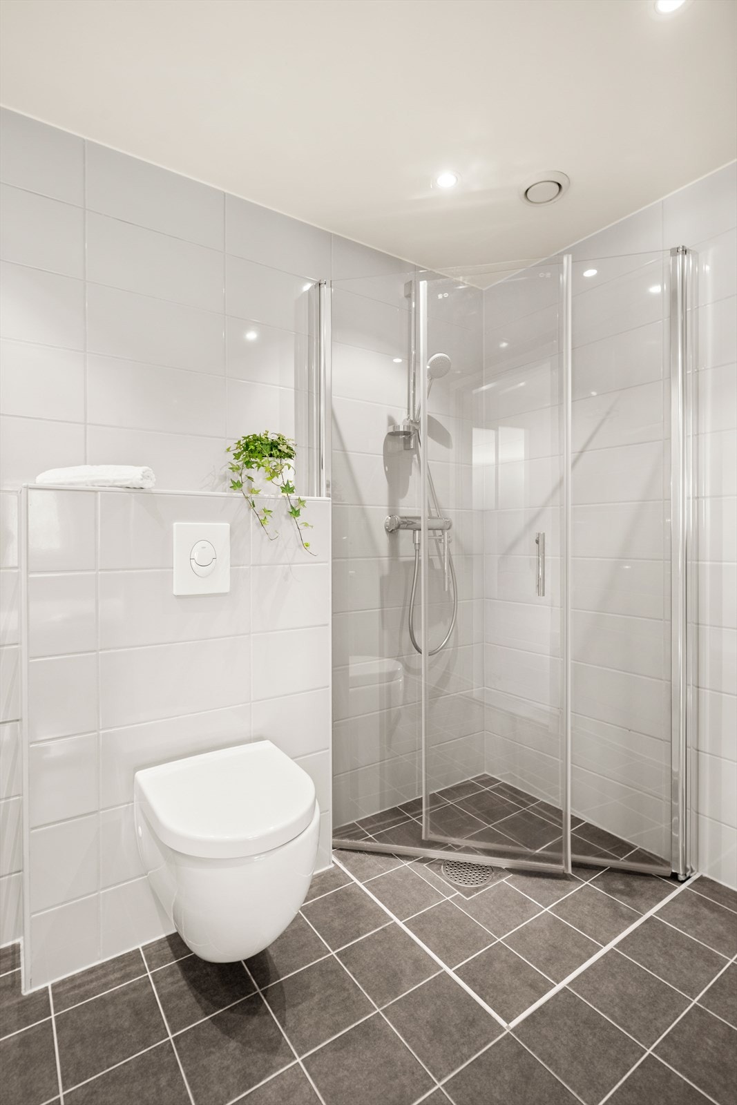 Badet er innredet med vegghengt toalett, dusjhjørne med svingbare glassdører og baderomsmøbel med skap, nedfelt servant og speil med belysning. Det er opplegg for vaskemaskin. Galleribilde