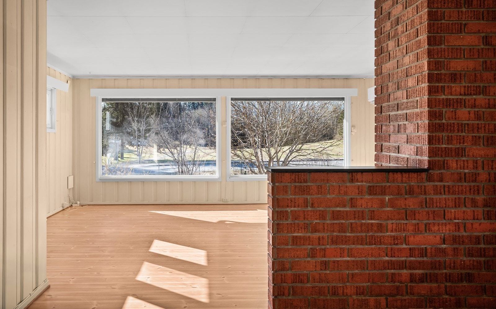 Rommet har tregulv og panel på veggene, og en murt pipe som et sentralt element. Galleribilde