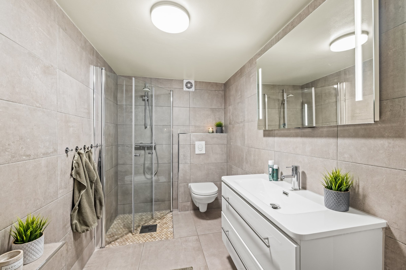 Badet er helfliset med vannbåren varme, vegghengt toalett og dusjhjørne med innfellbare dører. Galleribilde