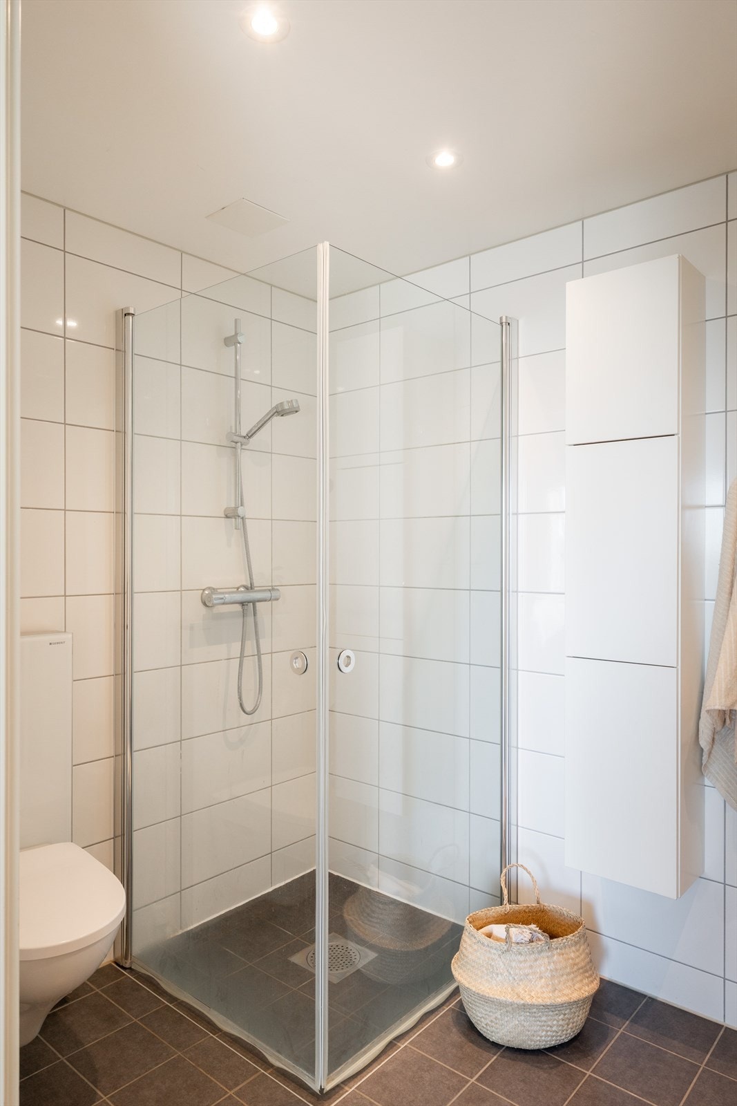 Badet er innredet med vegghengt klosett, servant med innredning, speilskap m/lys og dusjhjørne med svingbare glassdører. Galleribilde