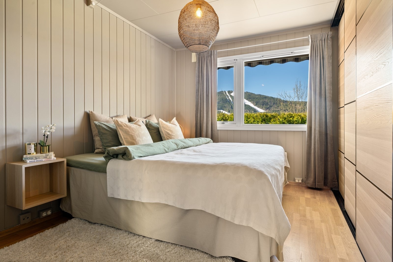 Hovedsoverommet med rolig og lun atmosfære, malt i en behagelig, dempet beige tone som gir et varmt uttrykk. Praktisk garderobeløsning gir god plass til oppbevaring, mens vinduet slipper inn rikelig med naturlig lys og gir utsyn mot de grønne omgivelsene. Galleribilde