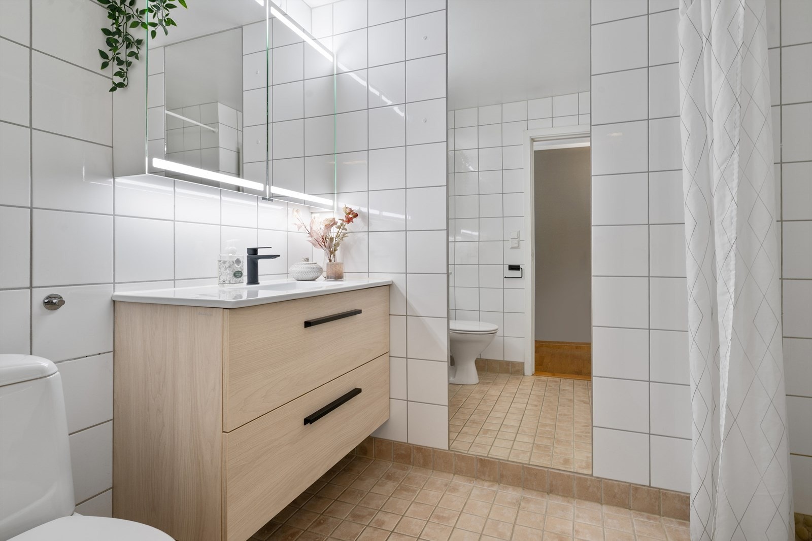 Pent flislagt bad med moderne servantseksjon, gode oppbevaringsløsninger og speil med integrert belysning. Rommet fremstår lyst og velholdt med nøytrale overflater og gjennomtenkte detaljer. Galleribilde