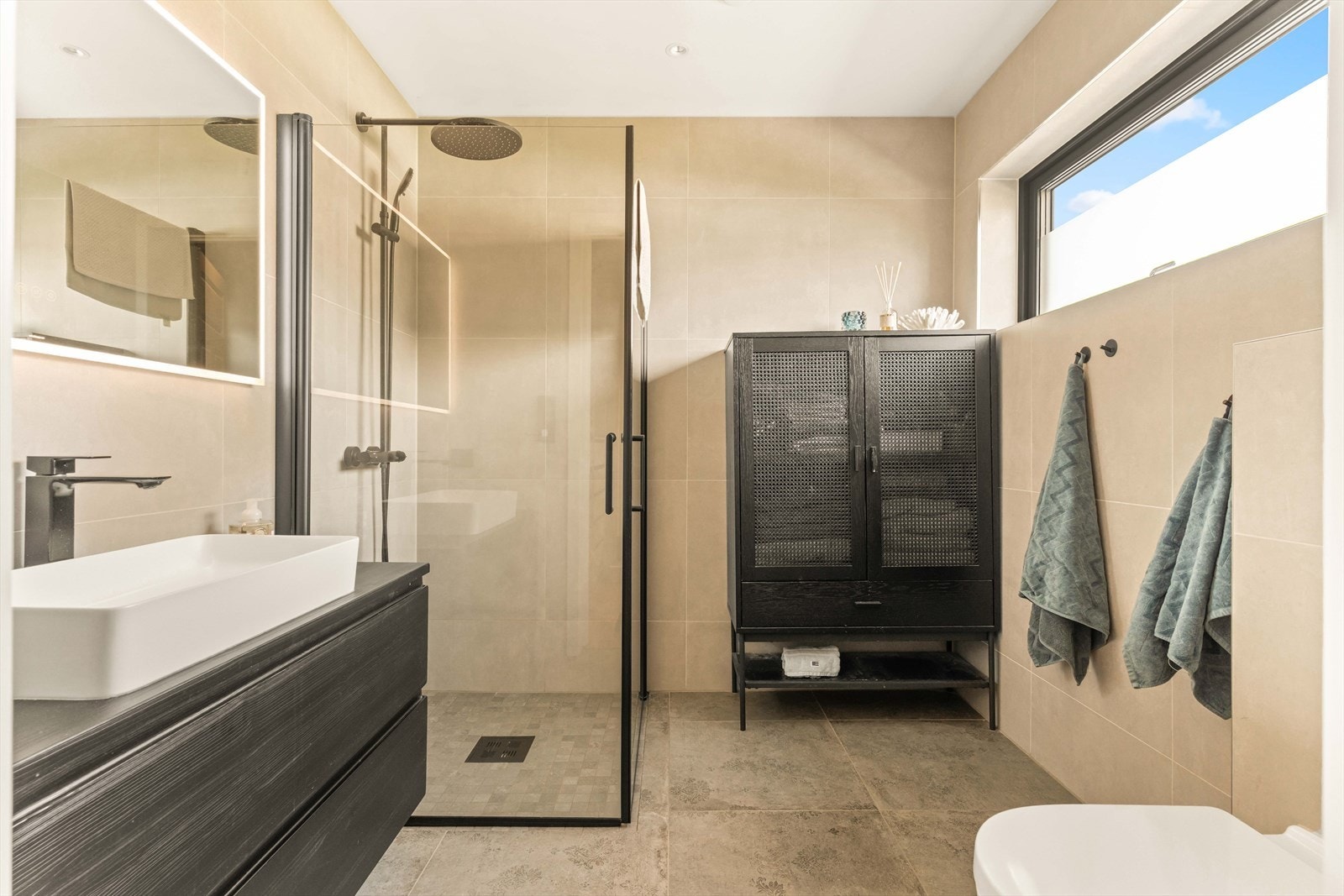 Badet er i delikat utførelse med store fliser i lun fargetone. Utstyrt med en romslig dusjnisje med glassdører og regnfallsdusj. Galleribilde