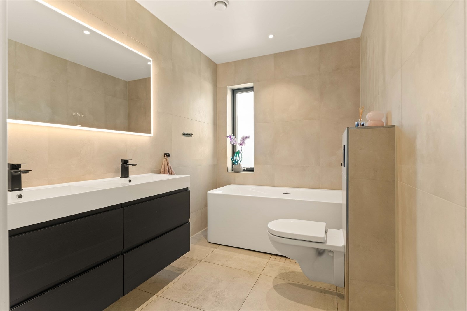Hovedbadet med inngang fra gang er elegant innredet med doble servanter, badekar og moderne, sorte armaturer. Galleribilde