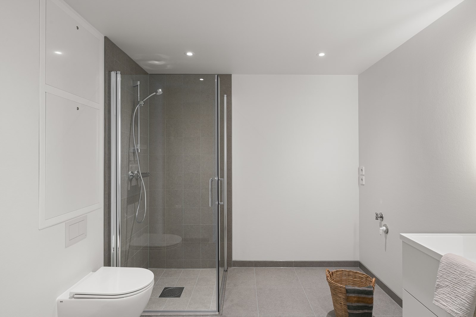Badet har moderne, grå fliser på gulv og i dusjsonen, samt opplegg for vaskemaskin. Galleribilde