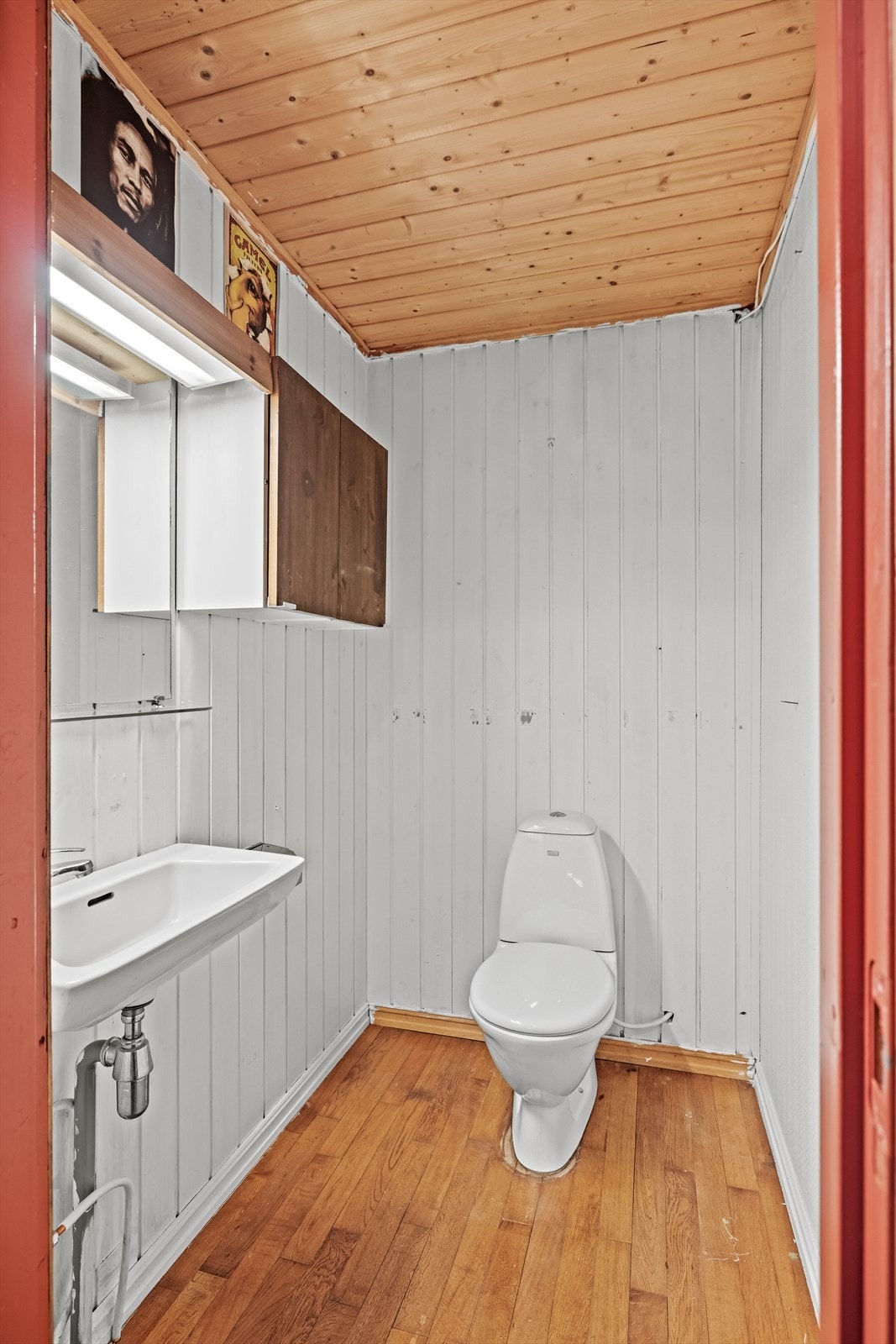 Toalettrom i kjelleren med parkett på gulv, panel på vegger, vegghengt servant og gulvmontert toalett. Galleribilde