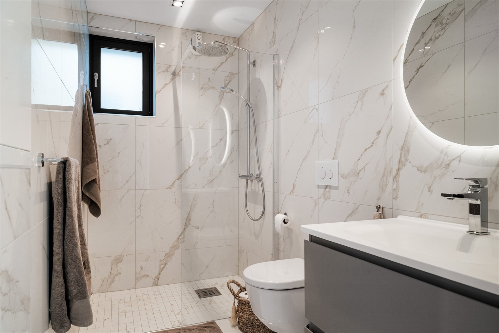 Bad i tidløst design med store marmorfliser, regnfallsdusj, downlights og speil med integrert belysning. Galleribilde