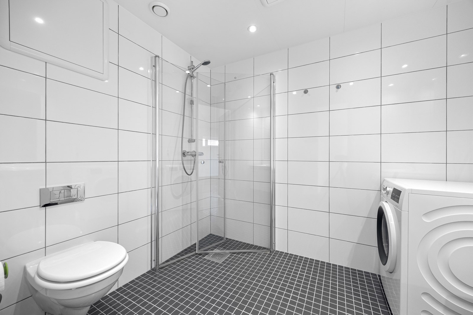 Badet er innredet med vegghengt wc, dusj med innfellbare dusjdører, baderomsinnredning med speil og opplegg til vaskemaskin. Galleribilde
