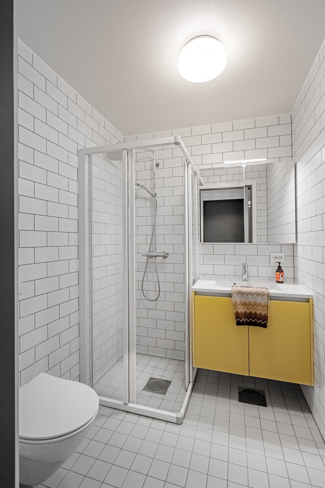 Badet i underetasjen er praktisk og moderne, med en nedfelt vask i en stilren skapseksjon, dusjhjørne og vegghengt toalett . Galleribilde