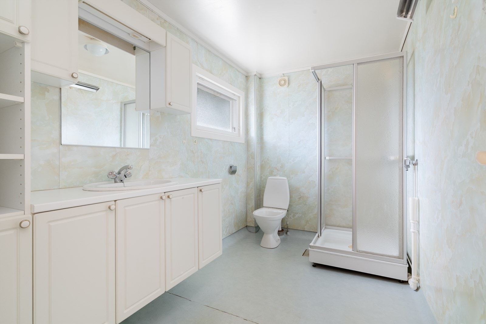 Badet har belegg på gulv, baderomsplater på veggene og er utstyrt med dusjkabinett, toalett, servantinnredning og opplegg for vaskemaskin. Galleribilde