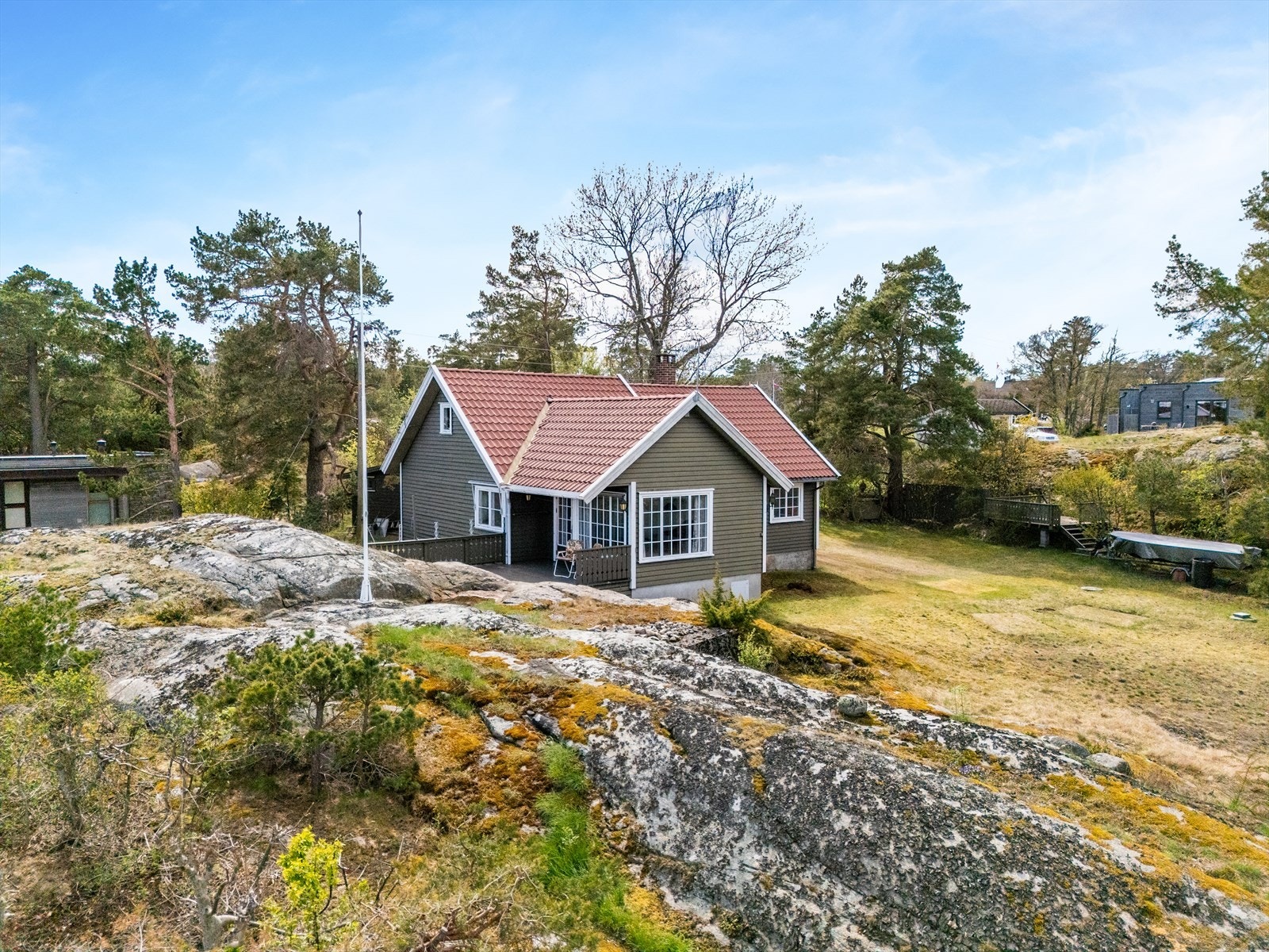 Tomten består av en kombinasjon av plen, naturtomt og svaberg. På baksiden av hytta er det satt opp et uthus med to boder. Galleribilde