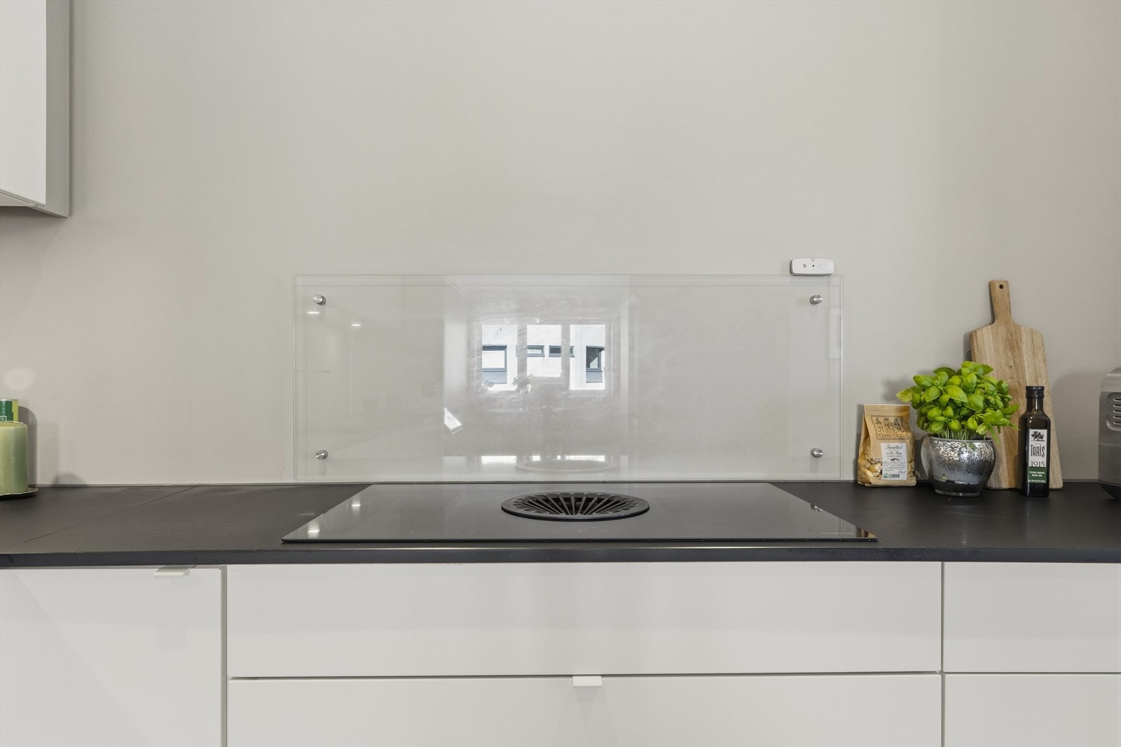 Backsplash i glass bak koketoppen. Benkeplate i kompaktlaminat i matt sort, nedfelt kum og integrert koketopp med kullfiltervifte. Galleribilde