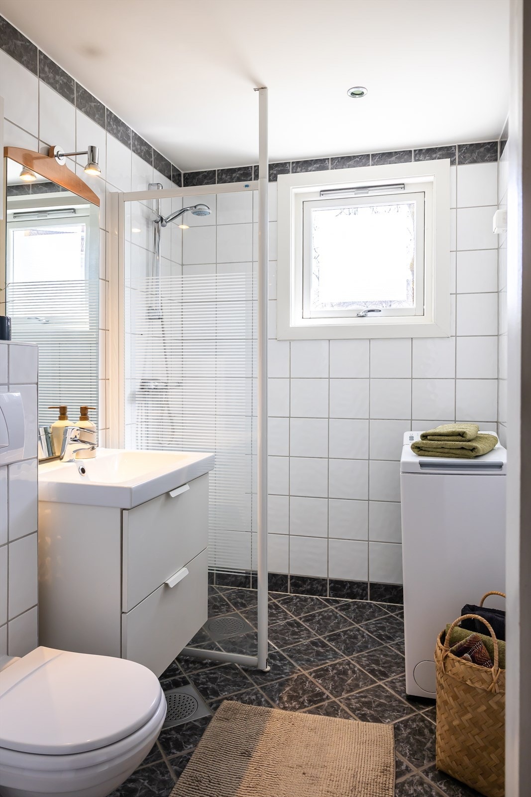 Tidløst flislagt bad med med varmekabler i gulv. Vegghengt toalett med innebygd sisterne kasse og vegghengt skap med servant fra 2020. Galleribilde