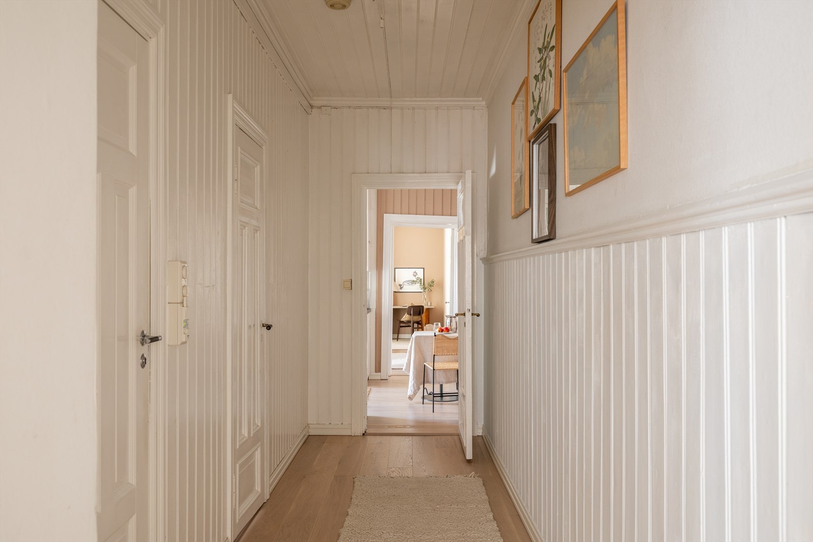 Mellomgang som tar deg fra oppholdsrommene og resten av leiligheten. Brystpanel på vegg og parkett på gulv. Galleribilde