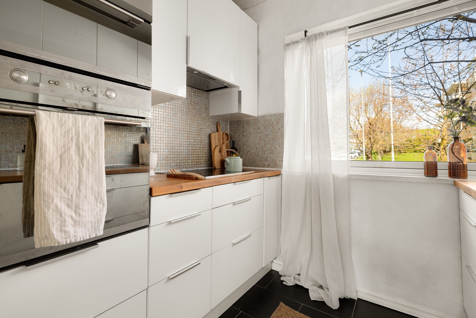 IKEA kjøkkeninnredning fra 2012 med glatte fronter, benkeplate i heltre med nedfelt kum i rustfritt stål, integrert platetopp, stekeovn og mikrobølgeovn. Galleribilde
