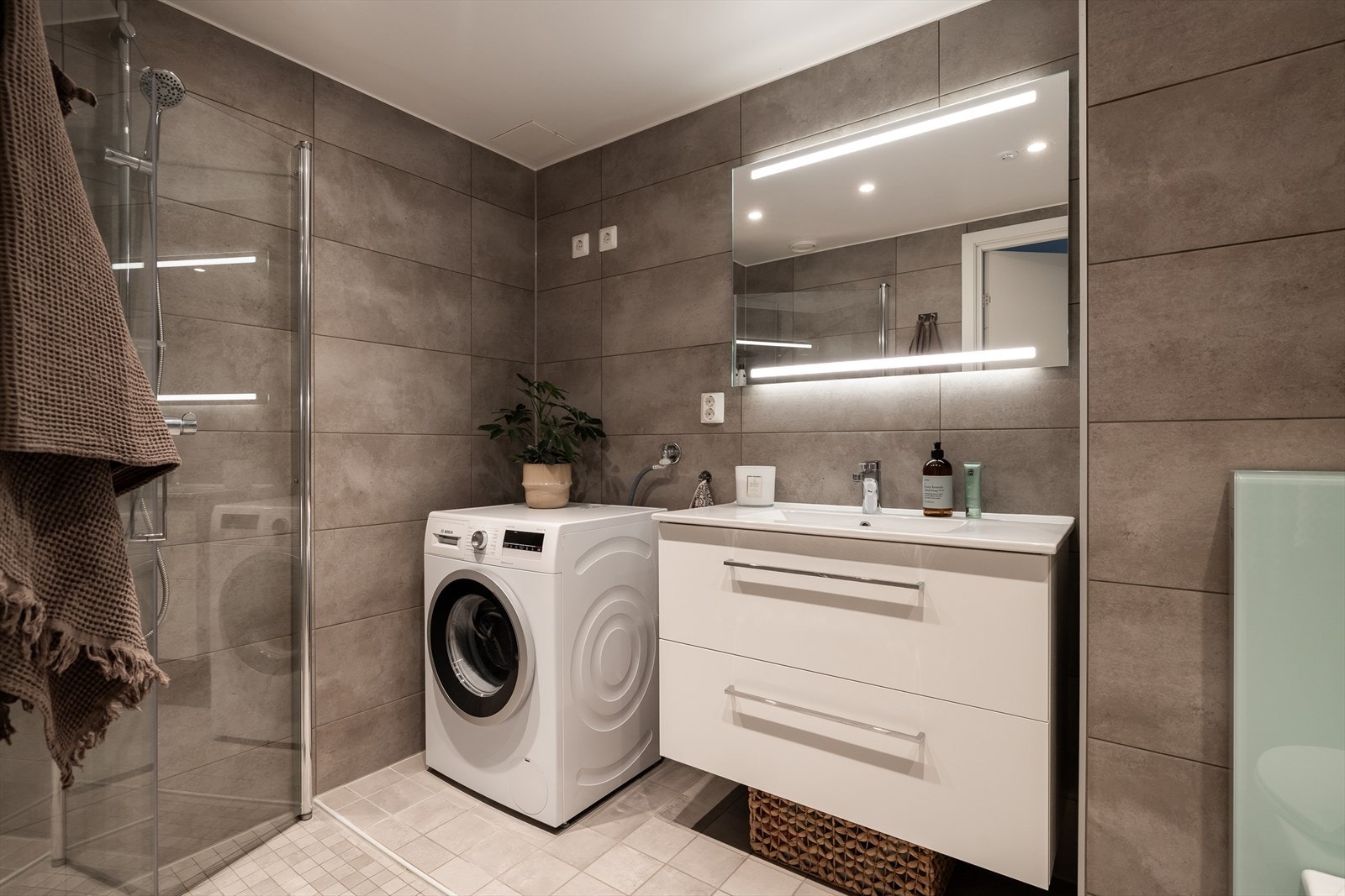 Lekkert og moderne flislagt baderom med god størrelse. Badet er innredet med delikat materialvalg og fremstår som svært delikat og tidsriktig. Praktisk opplegg for vaskesøyle gjør det enkelt å integrere vaskemaskin og tørketrommel. Galleribilde