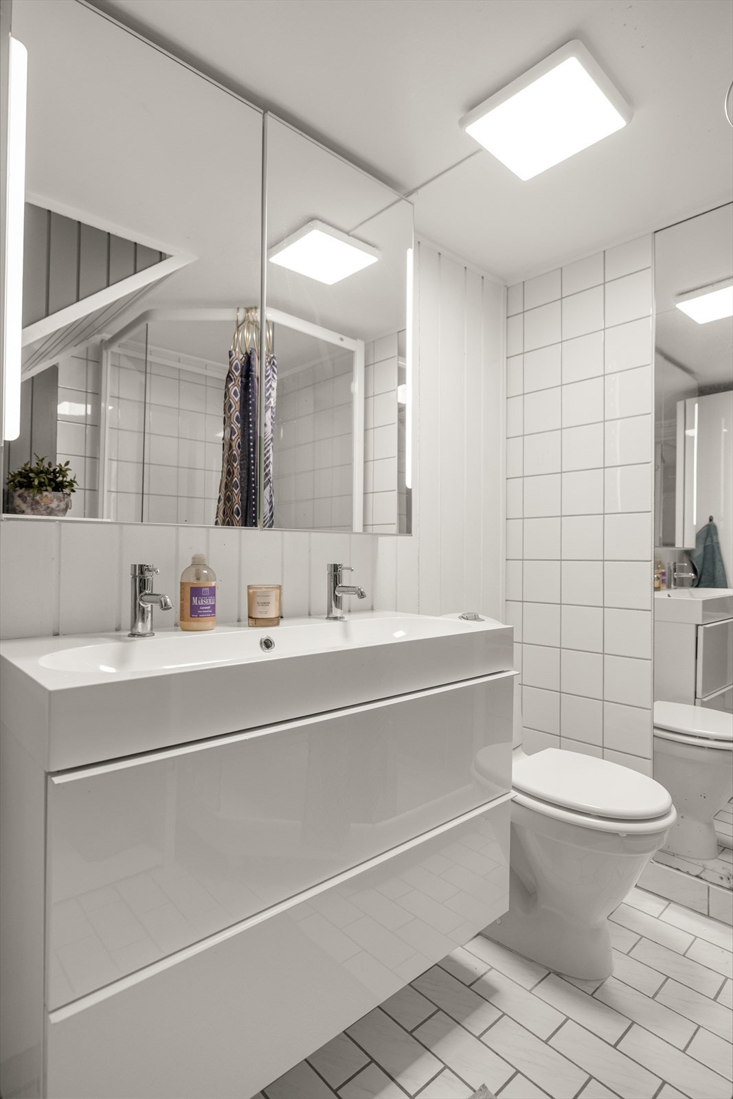 Badet er innredet med vegghengt servantinnredning, ovenpåliggende servant og armaturer, speilskap med belysning og stikkontakt på vegg over servant, vegghengt høyskap,
gulvstående toalett og dusjkabinett. Galleribilde