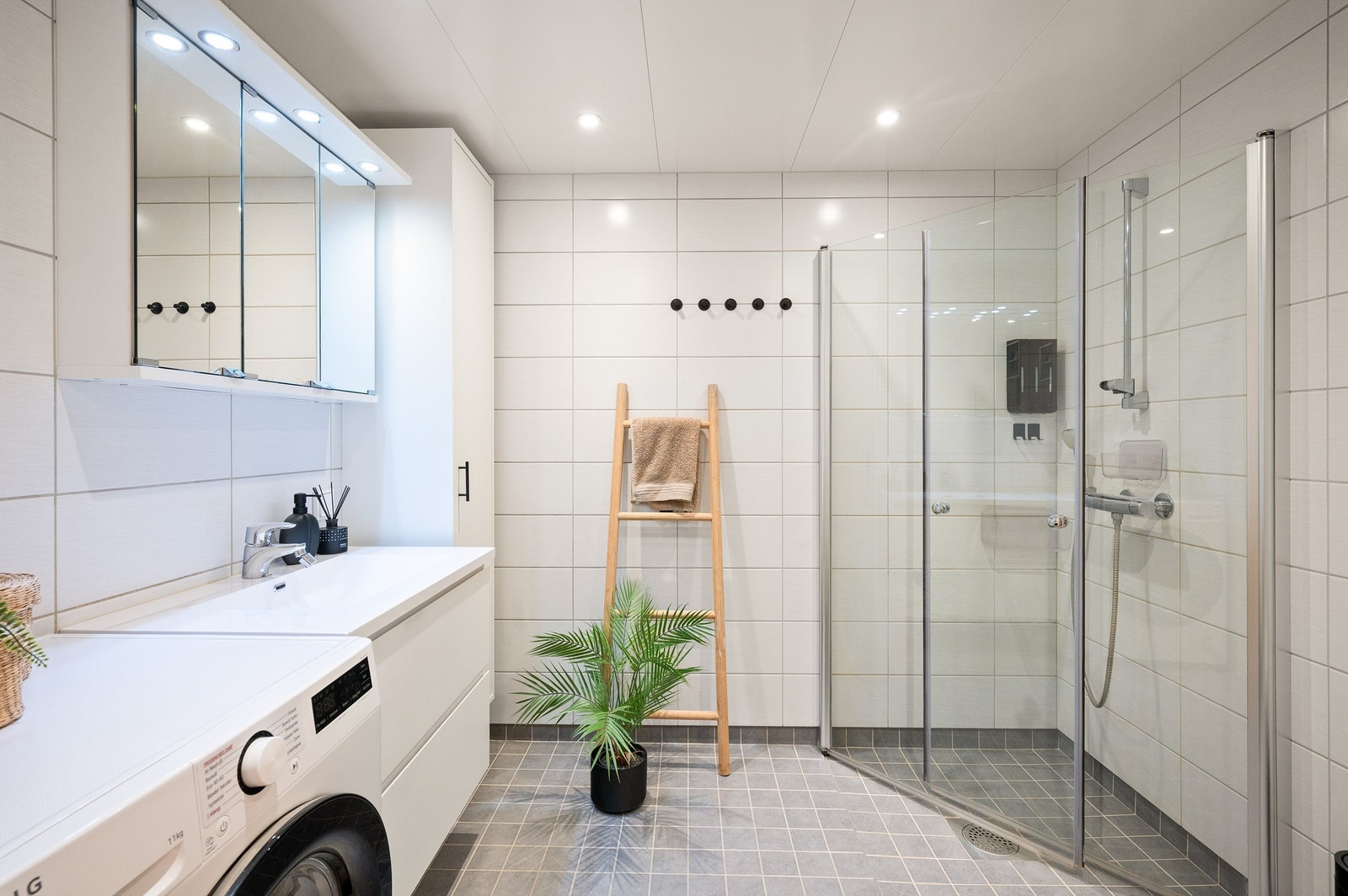 Innbydende og meget romslig bad med hvite fliser på vegg, gråmelerte fliser med varme i gulv og downlights i himling Galleribilde