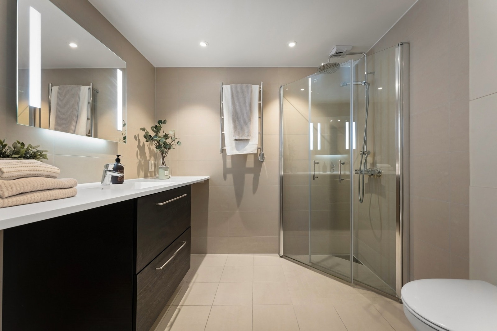 Badet er en prefabrikkert baderomsmodul fra 2022 og fremstår lekkert og moderne. Flislagte overflater, vannbåren gulvvarme og innfelte downlights i himling. Galleribilde