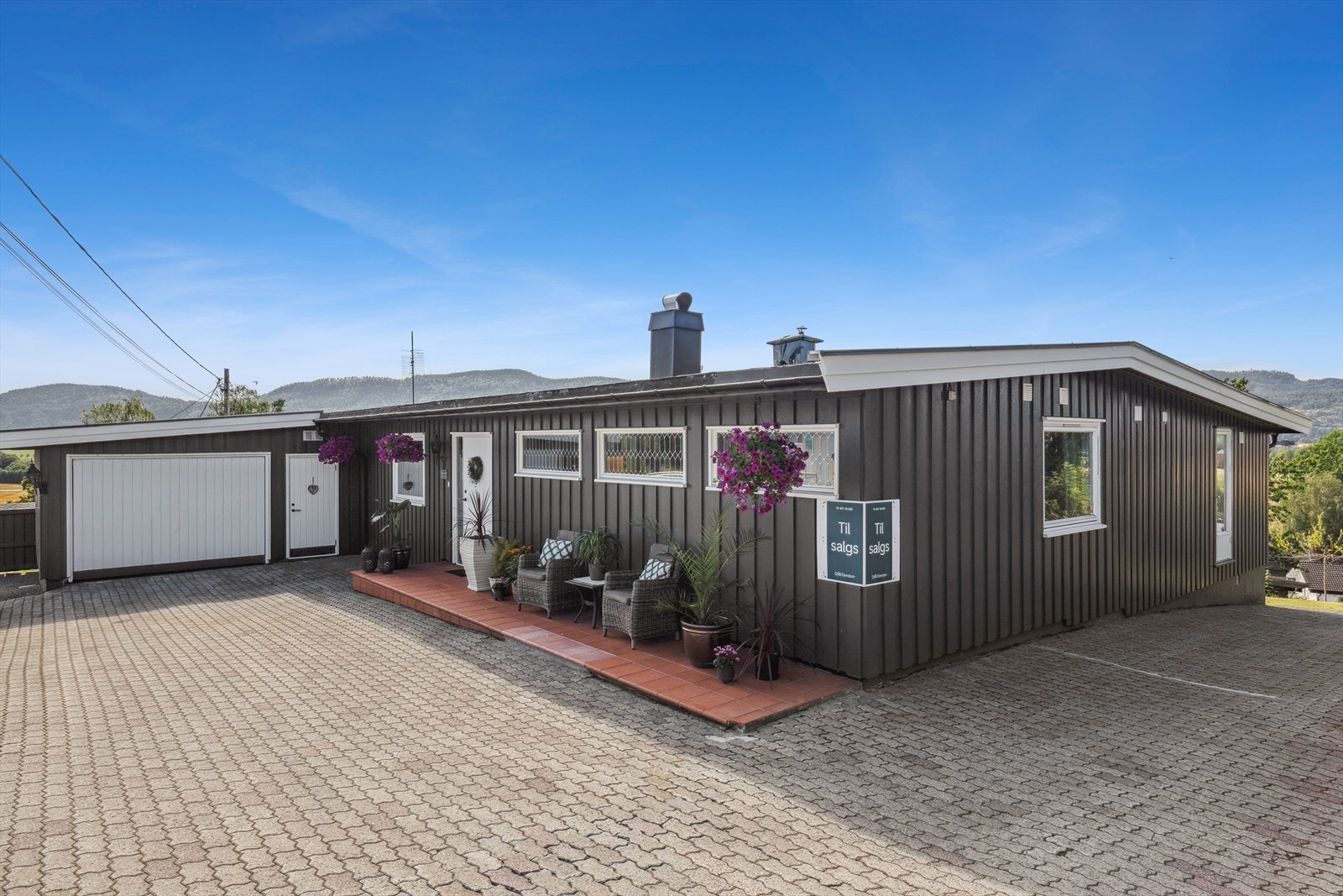 Stor steinbelagt gårdsplass med god plass for parkering, grusede gangstier og pene uteområder med plattingareal hvor solen kan nytes til det fulle. Garasje med med plass for parkering og utvendig bod. Galleribilde