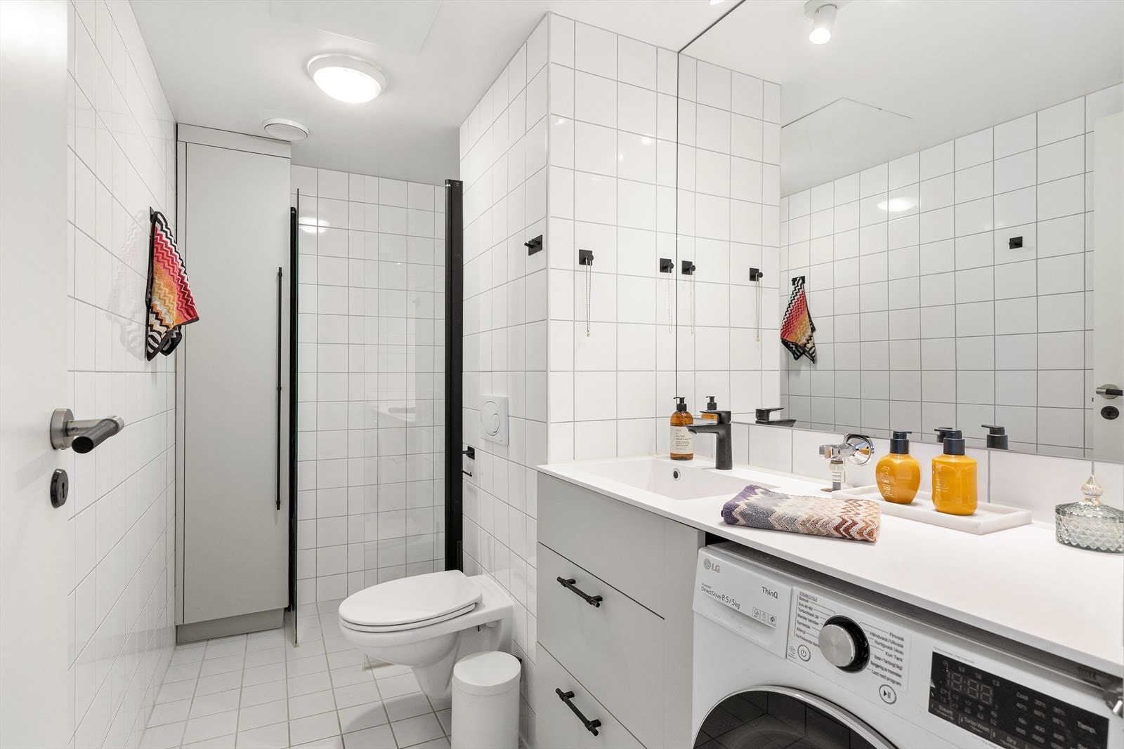 Badet er innredet med servantskap, benkeplate med nedfelt servant i corian og speil med belysning. Videre har badet vegghengt toalett og dusjsone med innfelte dusjdører i herdet glass. Galleribilde