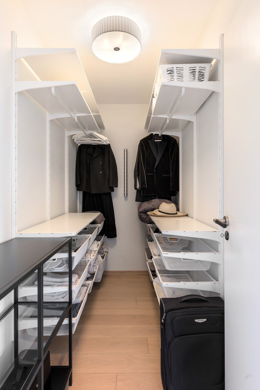 Praktisk og oversiktlig walk-in-closet med gode oppbevaringsløsninger. Rommet er innredet med åpne hyllesystemer og hengeløsninger på begge sider, som gir rikelig med plass til klær, sko og tilbehør. Galleribilde