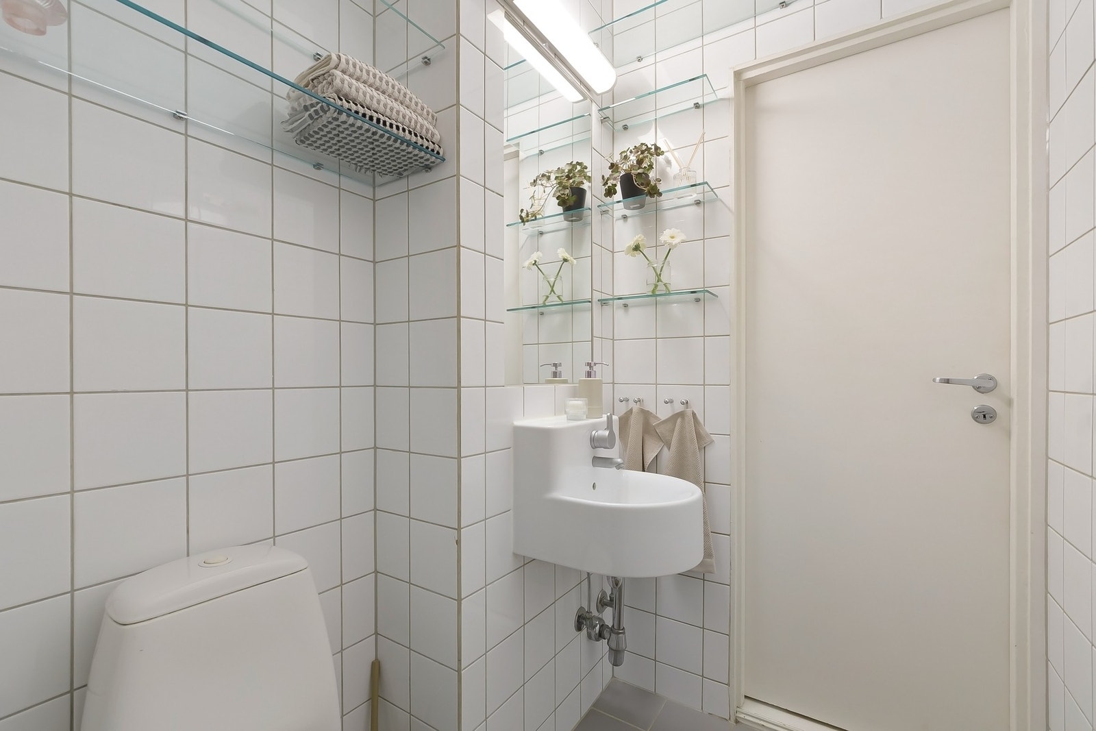 Badet er innredet med dusjnisje med skyvedør i herdet glass og justerbart dusjhode, servant og gulvstående toalett. Det er også glasshyller for oppbevaring av håndklær og toalettsaker. Galleribilde