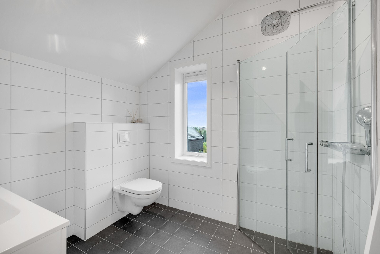Badet oppe er flislagt med gulvvarme, downlights, vegghengt toalett og et dusjhjørne Galleribilde