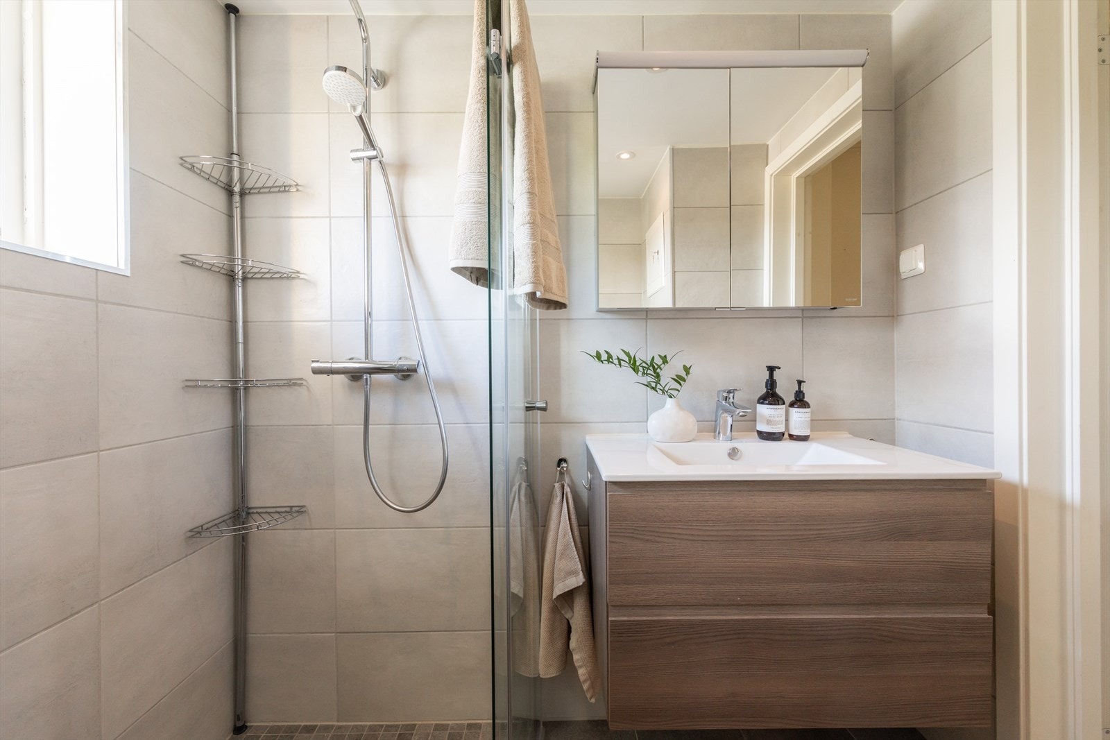 Badet er innredet med vegghengt toalett, servant nedfelt i innredning med gode oppbevaringsmuligheter, samt dusjhjørne med svingbare glassdører. Galleribilde