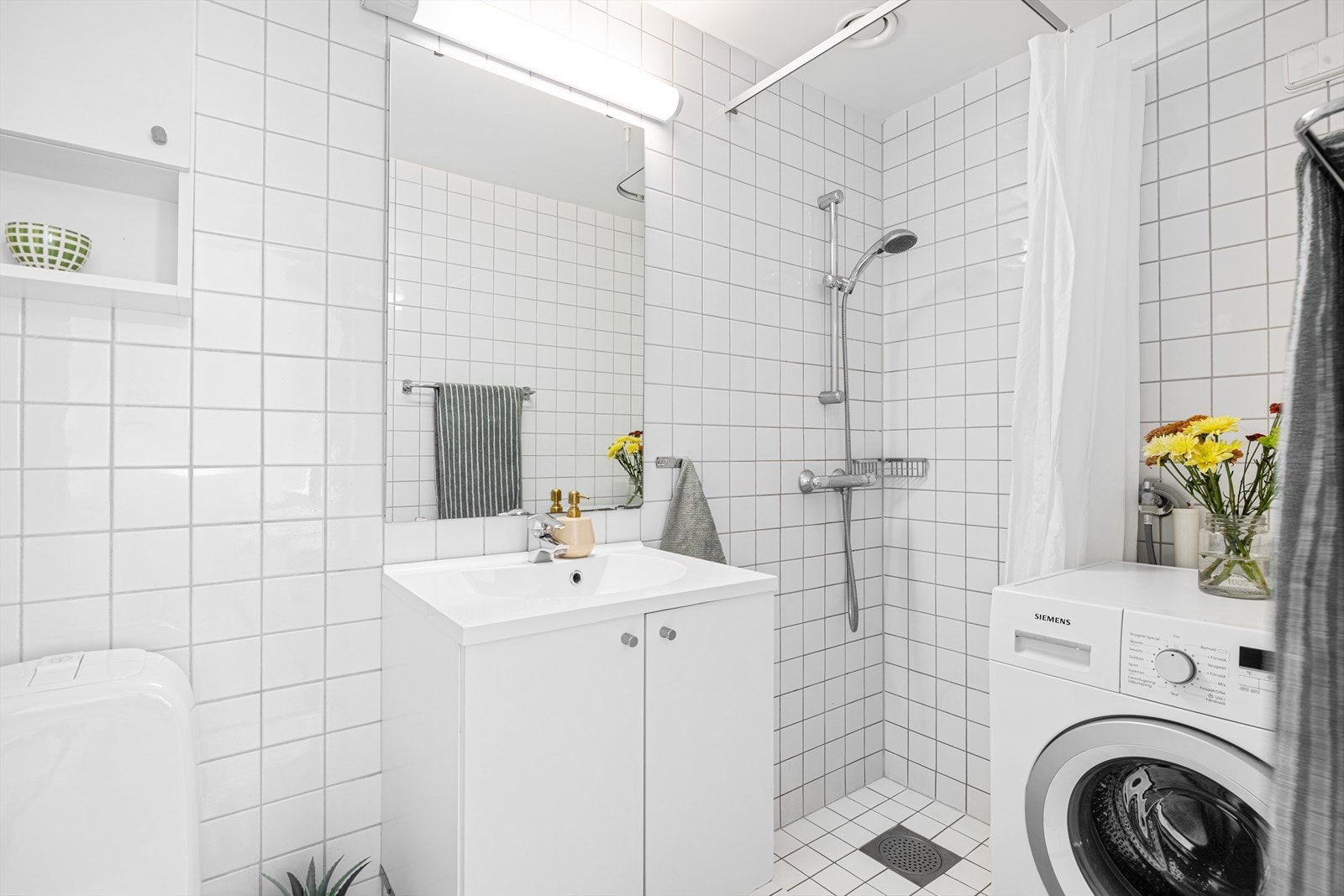 Flislagt bad med servantinnredning, toalett, dusj og opplegg for vaskemaskin Galleribilde