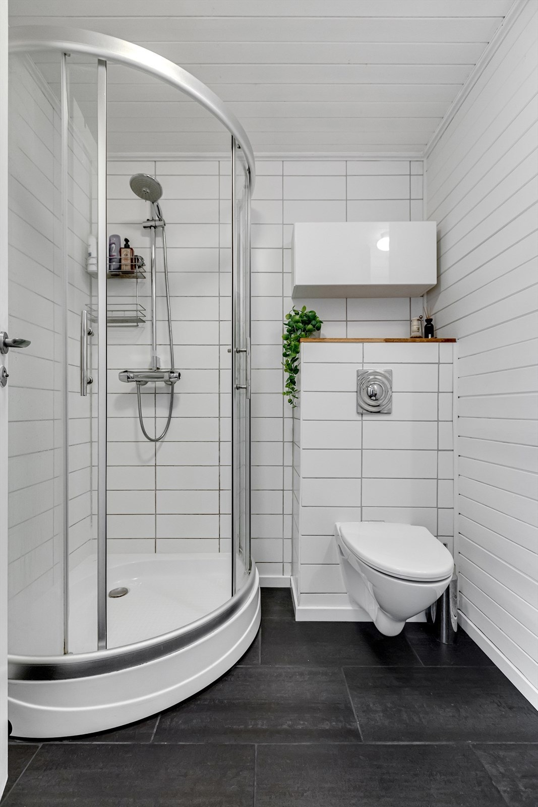 Badet er utstyrt med veggmontert toalett, dusjplass med dusjvegger og servant med ettgreps blandebatteri. Galleribilde
