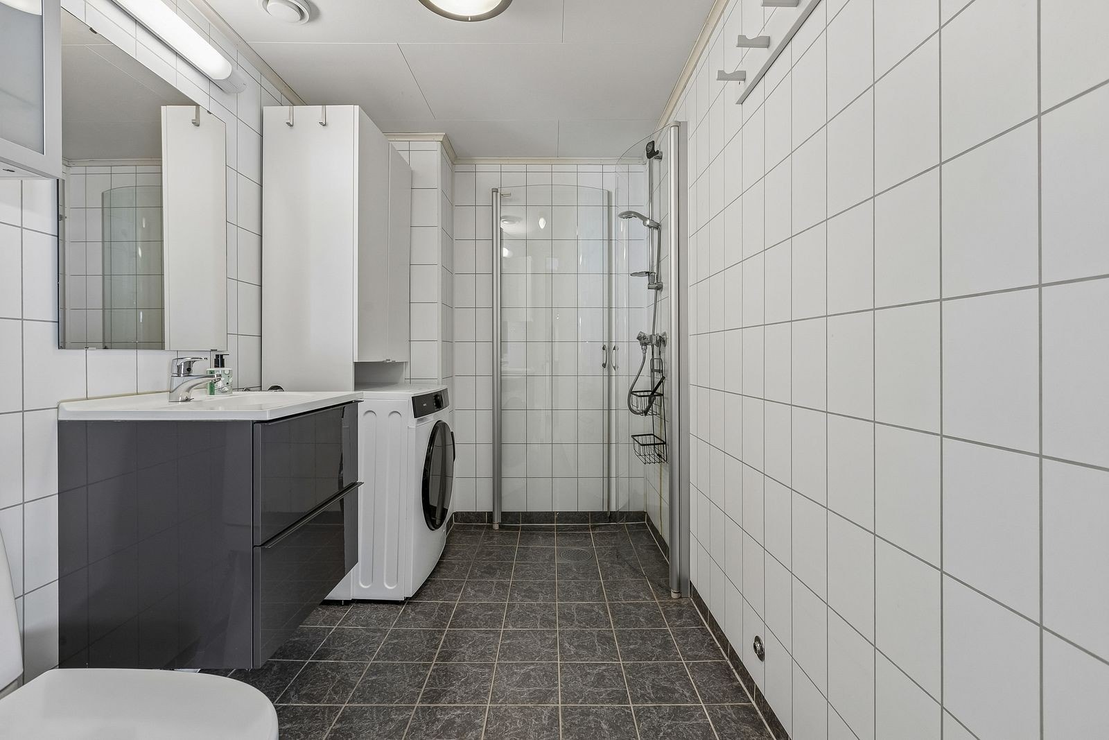 Lekkert flislagt bad med gulvvarme, dusjhjørne og opplegg for vaskemaskin. Galleribilde