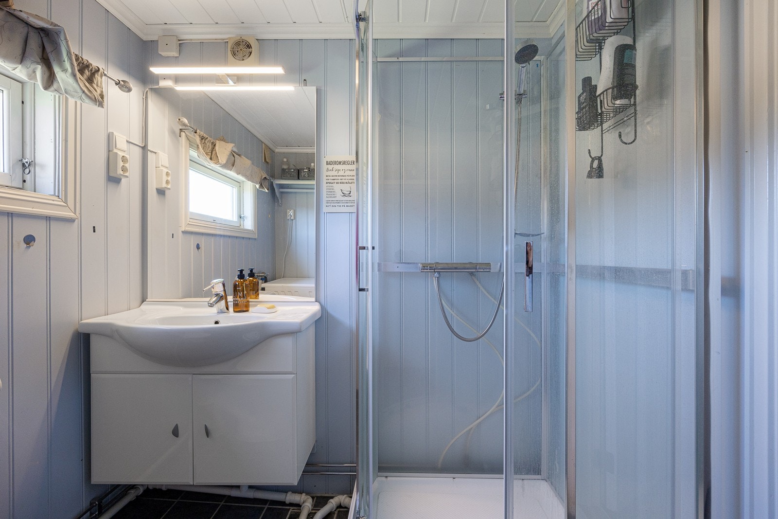 Badet er innredet med mørke gulvfliser og pastellblå panelplater på veggene. Galleribilde