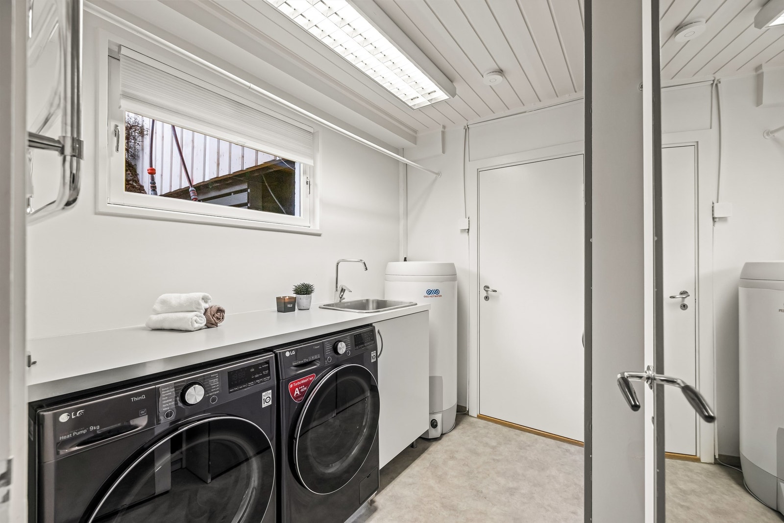 Praktisk og romslig vaskerom med opplegg for vaskemaskin, utslagsvask og god benkeplass. Her står også varmtvannsberederen fra 2018. Galleribilde