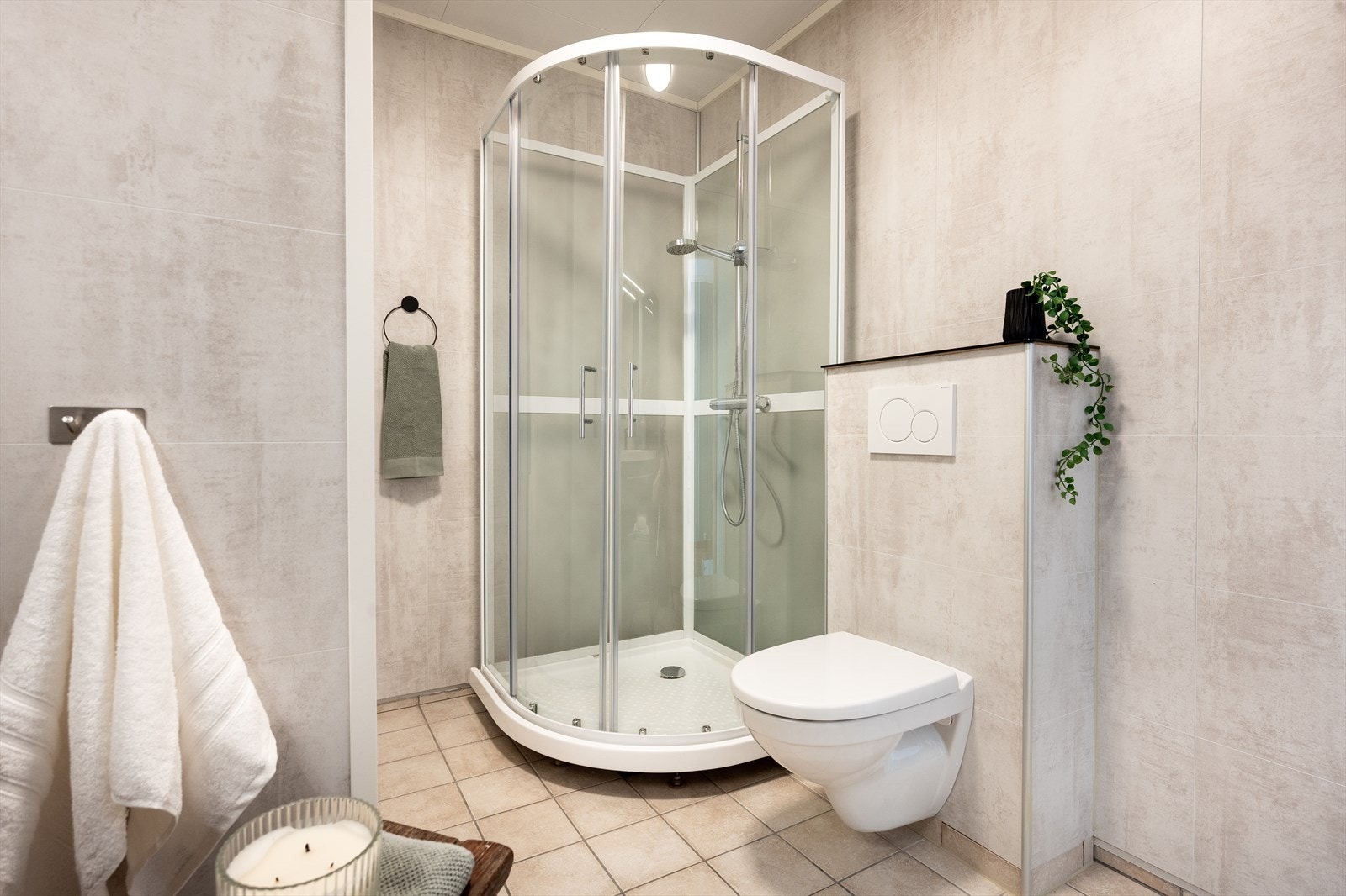 Badet er pent og funksjonelt, med flislagt gulv, våtromsplater på veggene og et buet dusjkabinett i hjørnet. Galleribilde